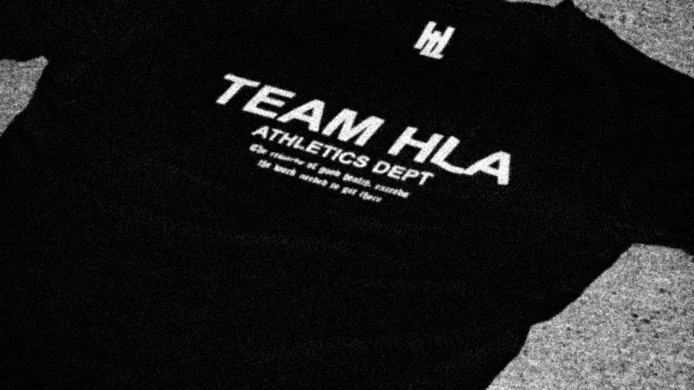 Sort TEAM HLA-t-skjorte flatlagt paa asfalt, 16:9